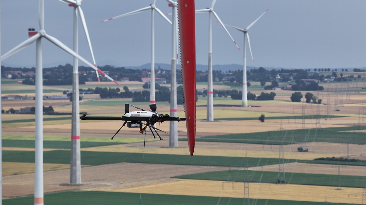 Voliro T Messdrohne im Einsatz an einem Rotorblatt, Windpark im Hintergrund